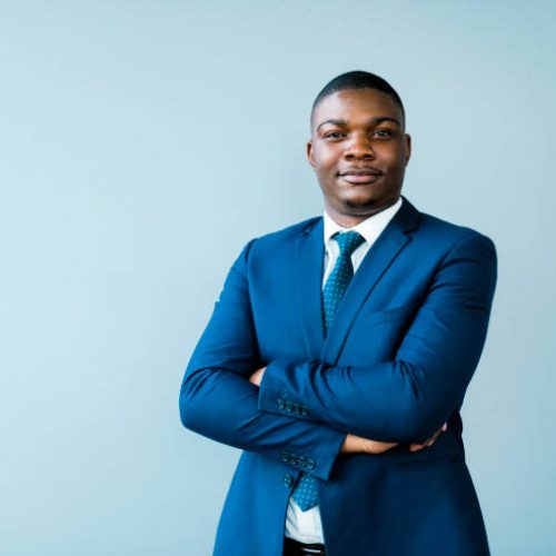 Portrait of confident businessman with arms crossed. Male entrepreneur is wearing blue suit. He is standing against gray background.